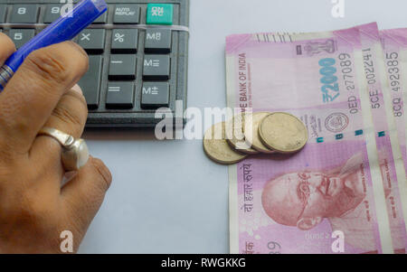 Cropped hand of a woman checking account with calculator and holding a pen. Indian currency notes and coins are on the side of table. Concept of home  Stock Photo
