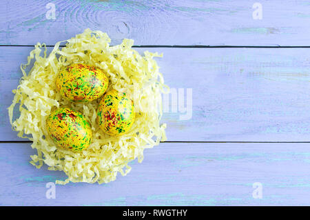 Colored easter eggs in yellow paper shavings. On blue wooden background. Stock Photo