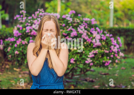 Young pretty woman blowing nose in front of blooming tree. Spring allergy concept Stock Photo