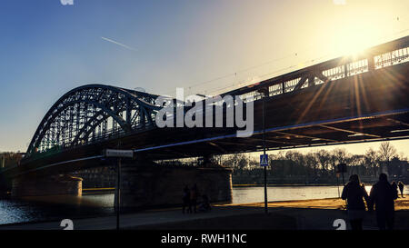 Krakow, Poland - February 16, 2019: People are walking along the Kurlandzki Boulevard next to the Pilsudski bridge in Krakow in the evening at sunset. Stock Photo