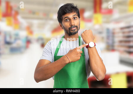 Indian manager man at hypermarket or supermarket showing wristwatch with index finger and angry expression as you are late concept Stock Photo