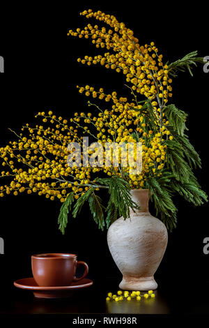Yellow mimosa flowers in a ceramic vase on a black table Stock Photo