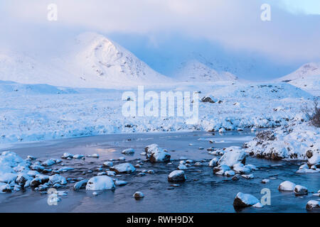 Cold winter morning with sun rising lighting mountains with frozen loch and snow at Loch Ba, Rannoch Moor, Argyll and Bute, Scotland in January Stock Photo