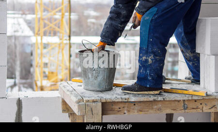 Professional worker laying brick in building construction. Yellow crane on the background. Stock Photo