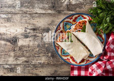 Typical Mexican burrito wrap with beef, frijoles and vegetables on wooden table. Copyspace Stock Photo