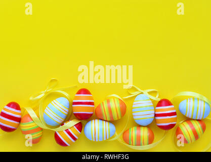 Colorful easter eggs and ribbons on a yellow background with empty space. Top view Stock Photo