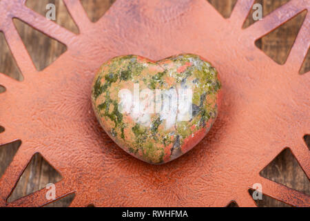 Highly polished puffy Unakite Heart from Unakas Mountains in North Carolina, on Rustic Orange decorative plate. Stock Photo