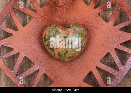 Highly polished puffy Unakite Heart from Unakas Mountains in North Carolina, on Rustic Orange decorative plate. Stock Photo