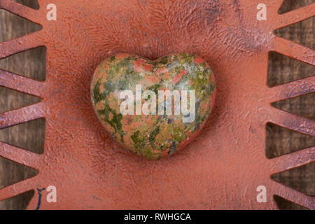 Highly polished puffy Unakite Heart from Unakas Mountains in North Carolina, on Rustic Orange decorative plate. Stock Photo