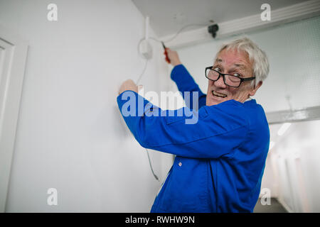 Senior electrician is fitting a security camera system in an office corridor. Stock Photo