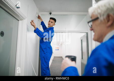 Trainee electrician is fitting a security camera with assistance from his tutor. Stock Photo