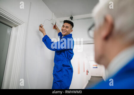 Trainee electrician is fitting a security camera with assistance from his tutor. Stock Photo