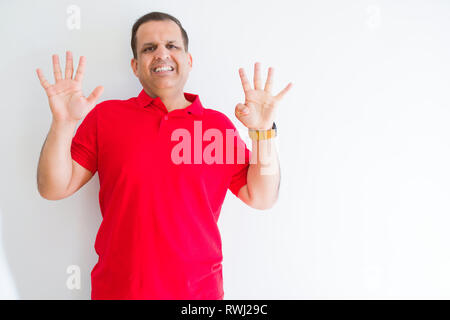 Middle age man wearing red t-shirt over white wall showing and pointing up with fingers number nine while smiling confident and happy. Stock Photo