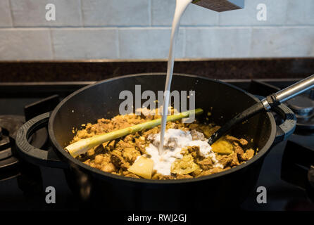 adding the coconut milk in a pan on the gas stove with indonesian rendang, a stew with beef Stock Photo