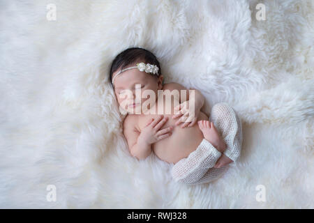 Sleeping, week old newborn baby girl wearing white, knitted pants. Shot in the studio on a white sheepskin rug. Stock Photo