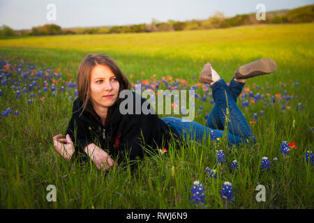 A young woman laying in a field of bluebonnet wildflowers; Waco, Texas, United States of America Stock Photo