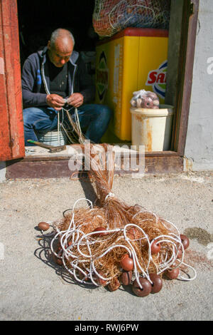 Fisherman repairing fishing net with cords and floats Stock Photo