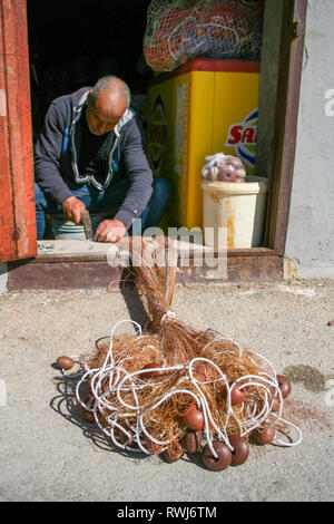 Fisherman repairing fishing net with cords and floats Stock Photo