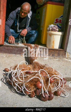 Fisherman repairing fishing net with cords and floats Stock Photo