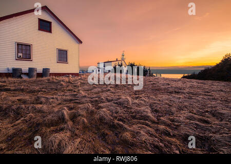 Sun setting behind the lighthouse at lobster cove head, Gros Morne National Park, Newfoundland and Labrador Stock Photo