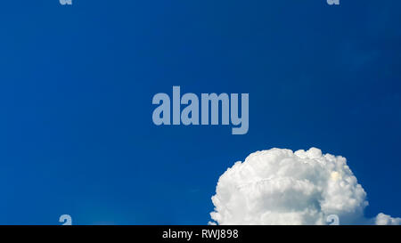 A fluffy and dense white cloud over a clean and blue sky in the bottom-right corner of the picture Stock Photo
