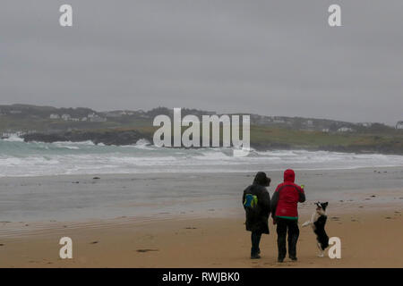 County Donegal, Ireland. 06 March 2019. Ireland weather - after heavy overnight rain, it was a day of strong winds and driving rain across County Donegal. Women playing with dog on wet and windy day on Dunfanaghy beach. Credit: David Hunter/Alamy Live News. Stock Photo