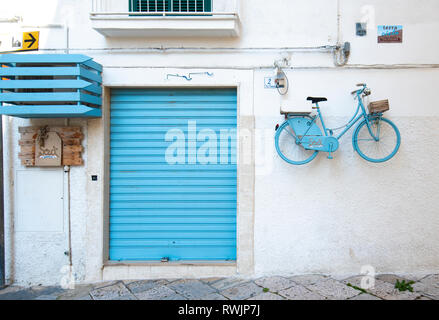 A blue door and a turquoise blue bicycle hanging on the wall in the old town of Monopoli, Puglia, Italy. A region of Apulia. Colorful house and street Stock Photo