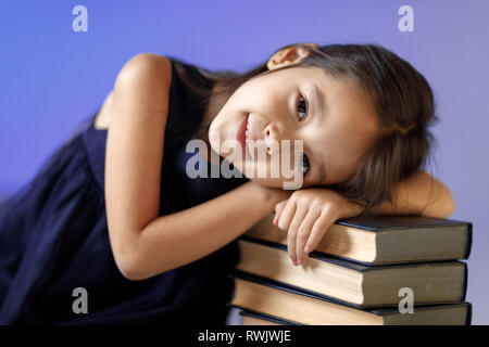 cute tired smiling little child girl in dark blue dress sleeping on reading books . Children and education. Stock Photo