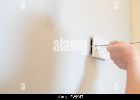 Electrician fitting double socket to stud wall Stock Photo