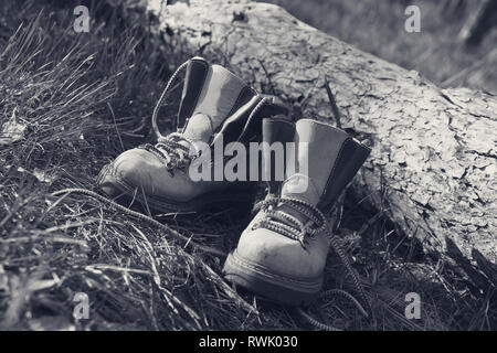 Pair of trekking boots in forest near fallen tree. Black and white retro toned image. Stock Photo