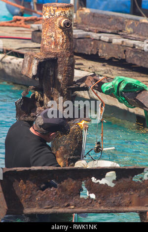 Men at work: worker deconstructing an old and broken steel pier standing in the open sea Stock Photo