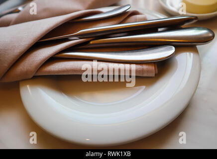 Table setting in the restaurant. White plate with  cutlery in napkin on a marble background Stock Photo