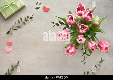 Springtime flat lay with bunch of pink tulips, eucalyptus leaves and gift boxes on stone surface Stock Photo
