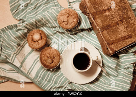 Flat lay of a snack with muffins, a cup of coffee and an old book on a green improvised doily Stock Photo