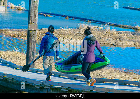 Young Asian couple carrying an inflatable kayak along a wooden ramp. Grant Narrows Regional Park, Pitt Meadows, British Columbia, Canada Stock Photo