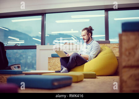 software developer writing programming code using laptop computer while sitting on lazy bag in modern startup office Stock Photo