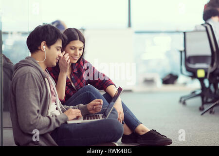 young software developers couple using laptop computer writing programming code while sitting on the floor at modern creative startup office Stock Photo
