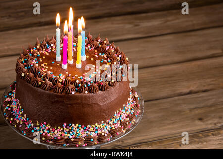 Chocolate birthday cake with colorful sprinkles and candles over wooden background. Stock Photo