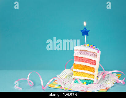 Slice of  birthday cake on a blue background with colourful layers and candle. Stock Photo