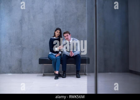 young business couple using smart phone while sitting on the bench at office lobby during a break Stock Photo