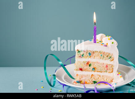 Slice of Birthday Cake with a lit candle and ribbons over a blue background. Stock Photo