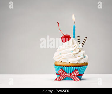 Cupcake with vanilla buttercream icing, birthday candle and a cherry on top. Stock Photo