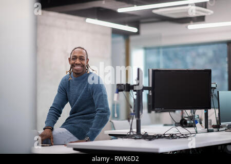 Portrait of young smiling african american male software developer sitting on office desk at modern startup office Stock Photo