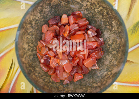 Moss Agate hand carved polished bowl from Morocco with tumbled Carnelian chips from Brazil in the middle of a circle made of colorful parrot feathers. Stock Photo