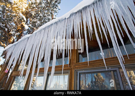 Giant icicles hang from an overhanging roof eave on a wooden house in Bend, Oregon, after a major winter snowfall. Stock Photo