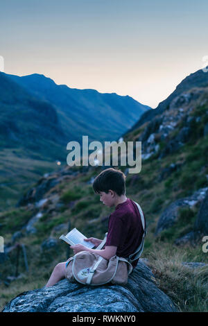 Boy reading book on hilltop, Snowdonia, Llanberis, Gwynedd, UK Stock Photo