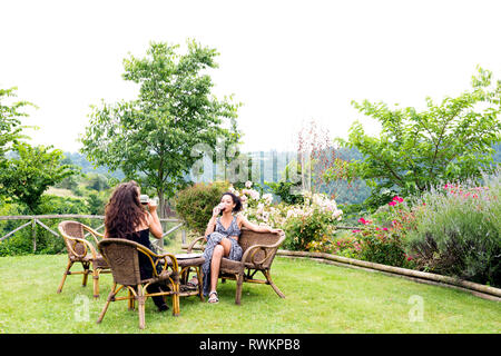 Women on wicker chairs in countryside garden, Città della Pieve, Umbria, Italy Stock Photo