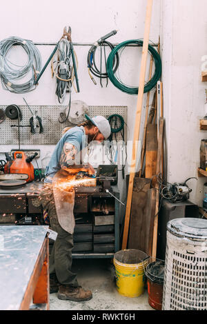 Axe maker using steel grinder in workshop
