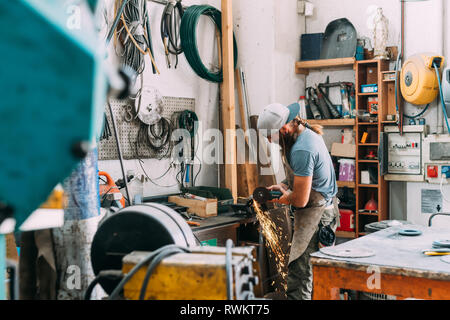 Axe maker using steel grinder in workshop Stock Photo