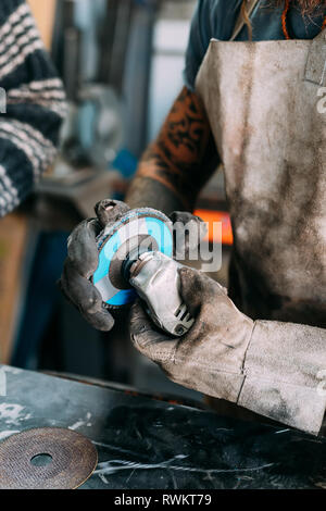 Axe maker using steel grinder in workshop Stock Photo